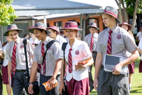 Four high school students walking outside. There is a group of students walking behind them in the background.