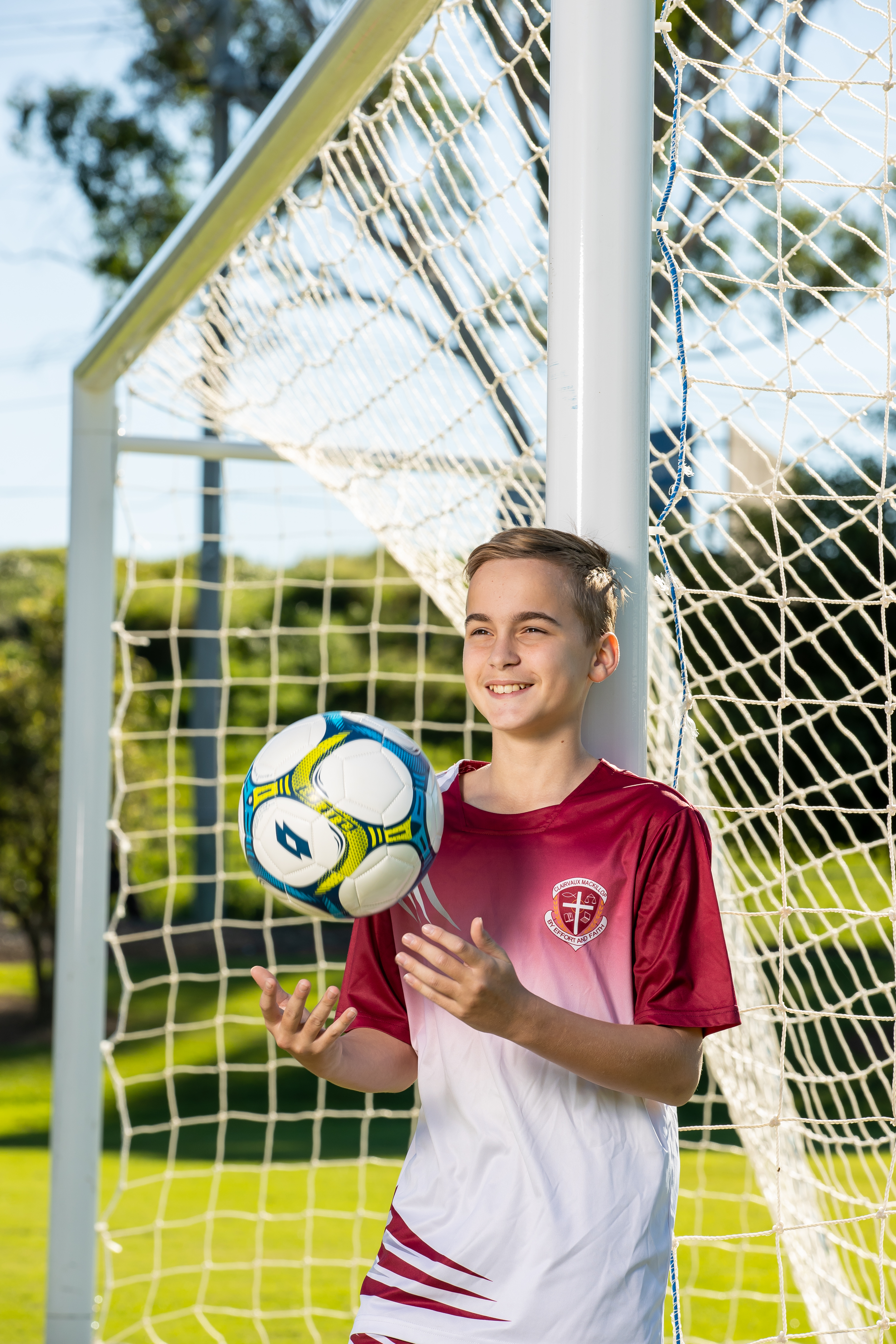 Student wearing a football jersey and standing in the goals. He is holding a football.