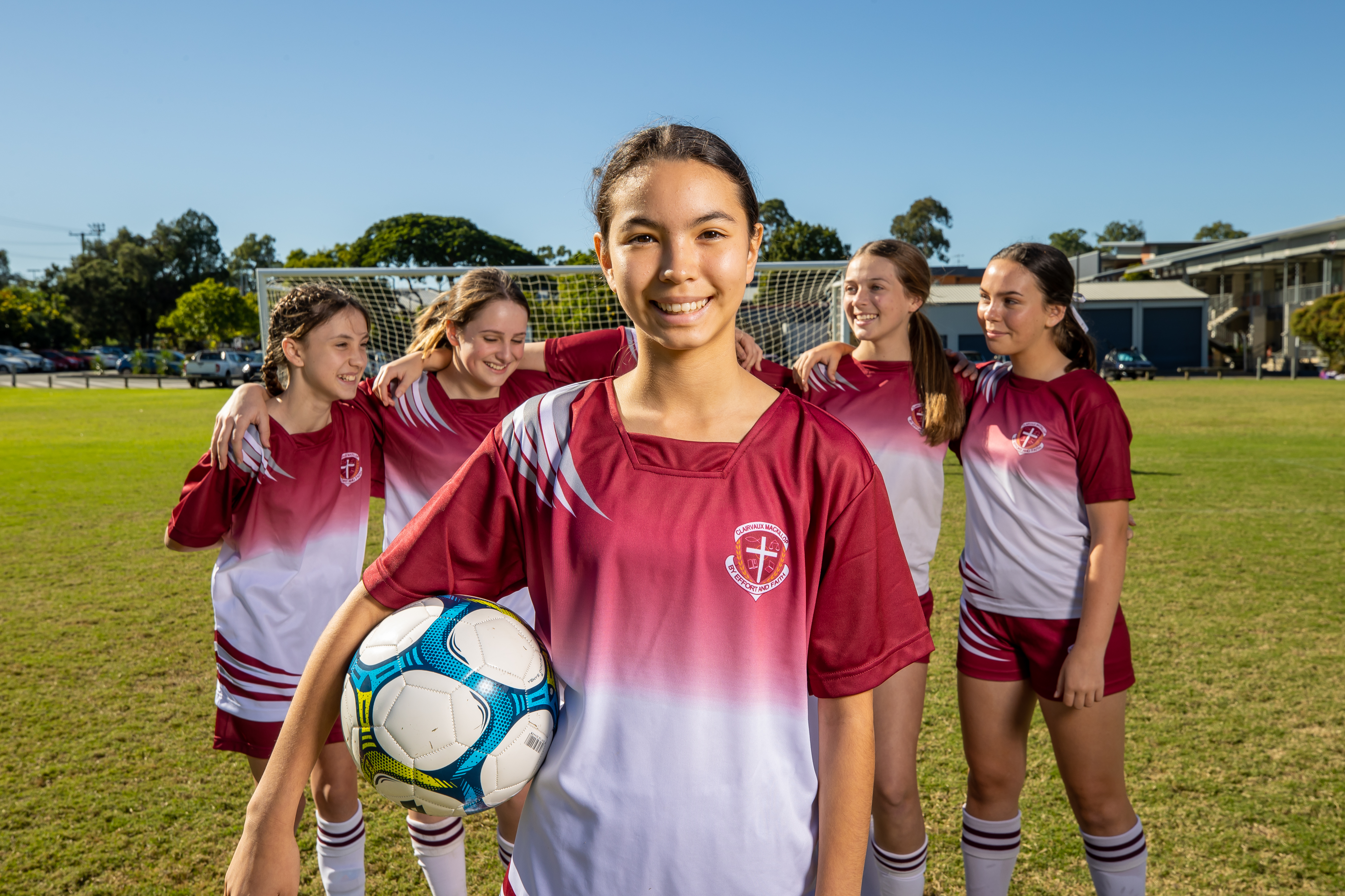 A student is facing towards the camera, holding a football. There are four students behind her with arms around each other.