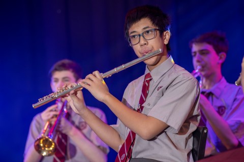 Student playing the flute at a concert. There are two students playing instruments in the background.