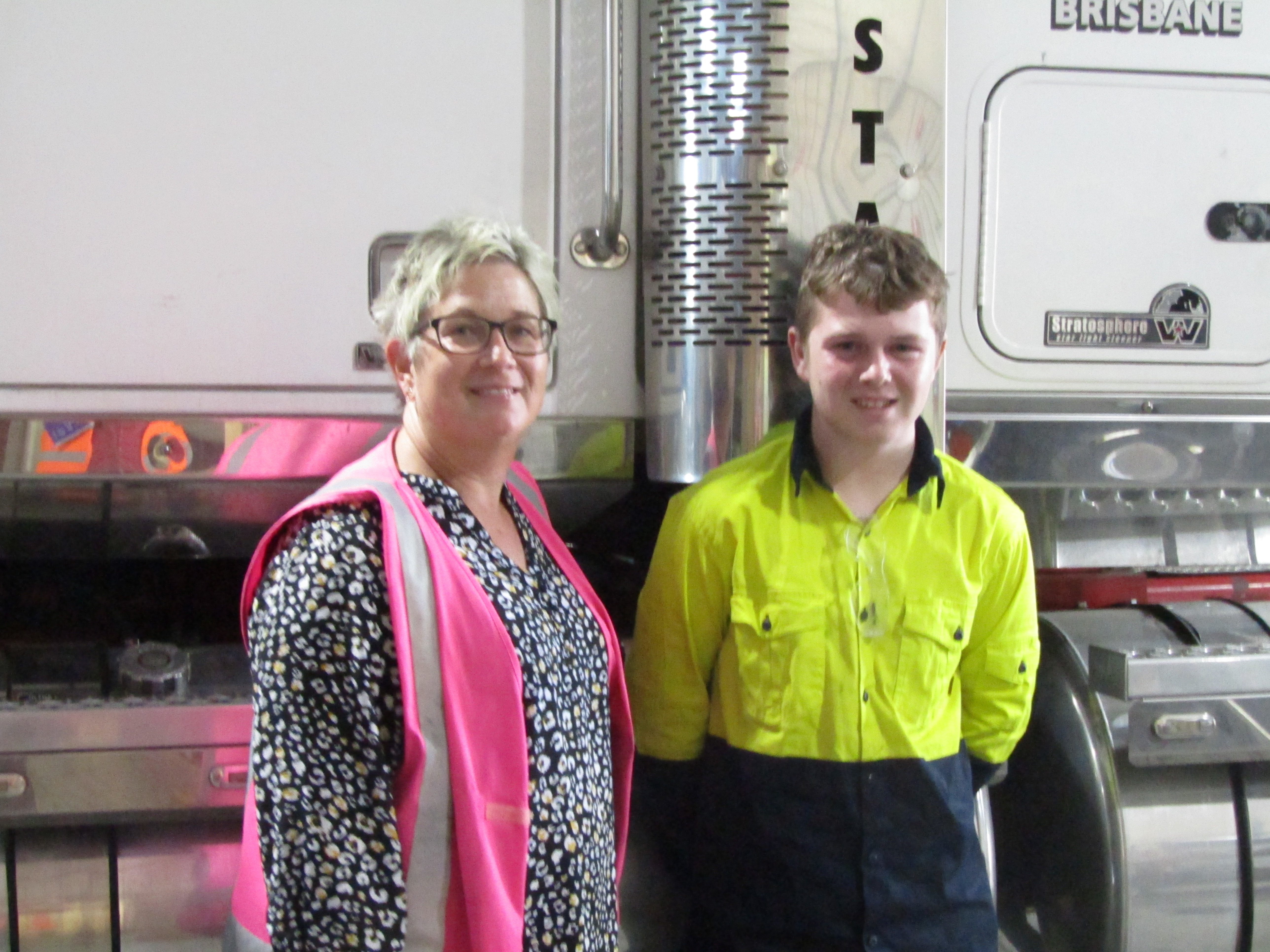 Student standing next to mentor in front of a large truck.