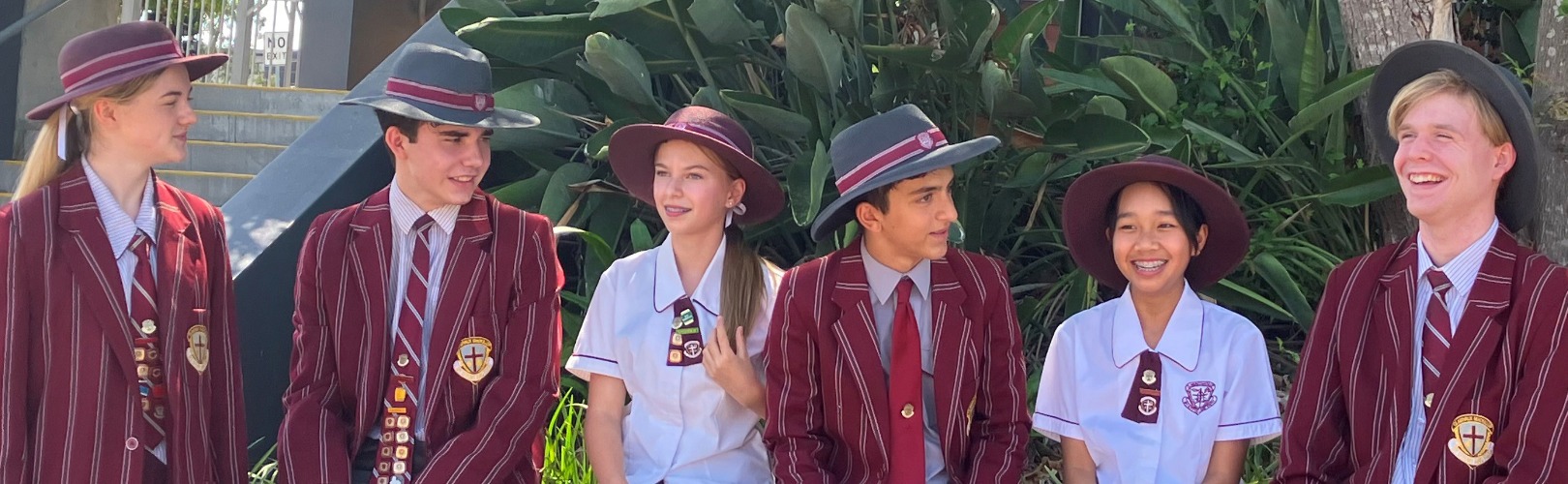 Six students wearing school uniform and standing in a line outside.