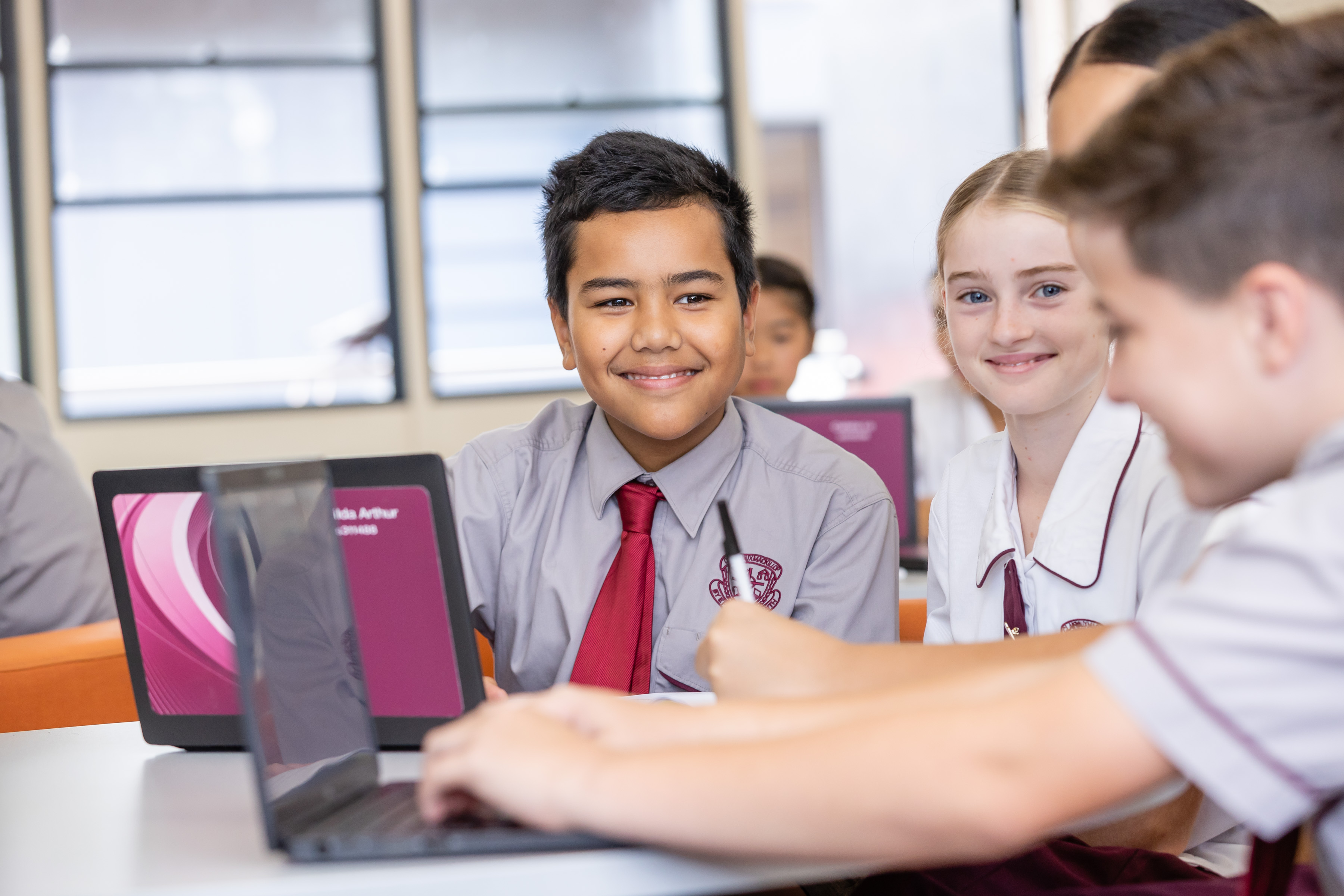Students are sitting at a desk with laptops.
